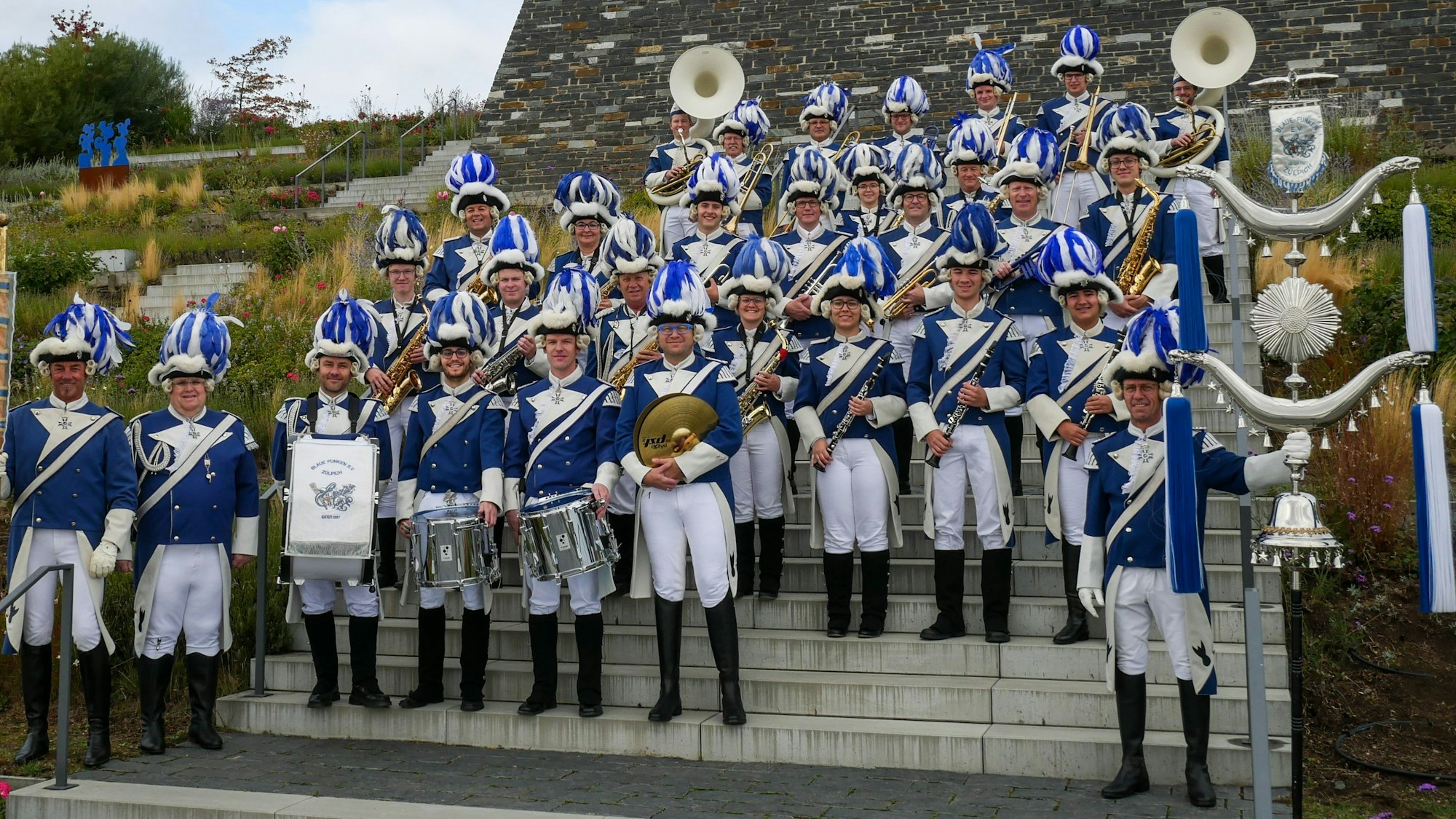 Das Bild zeigt den Musikzug der Blauen Funken auf dem Gelände des Seeparks in Zülpich. Sie stehen auf einer Treppe.