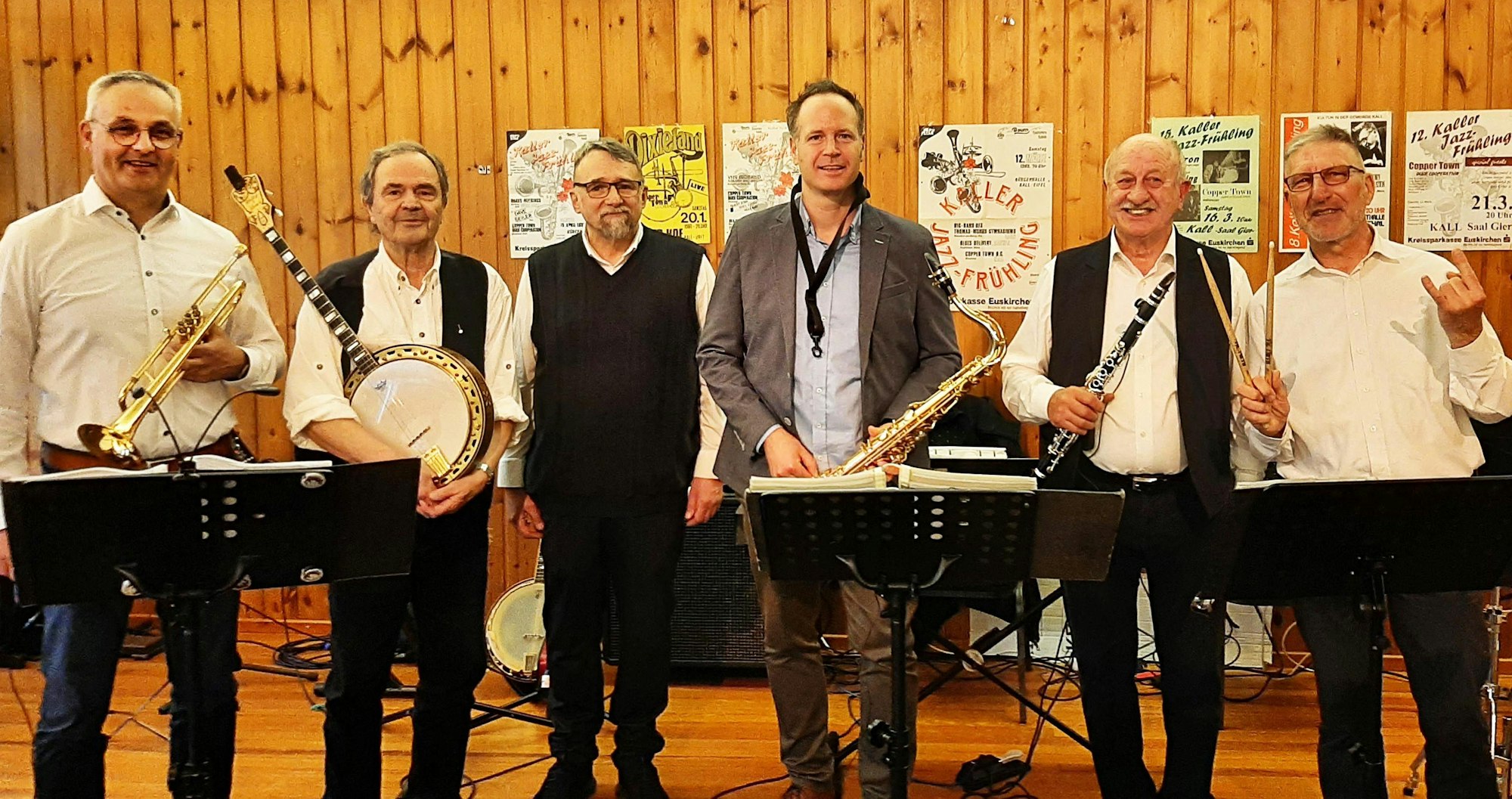 Die sechs Mitglieder der Band stehen nebeneinander und halten verschiedene Instrumente.