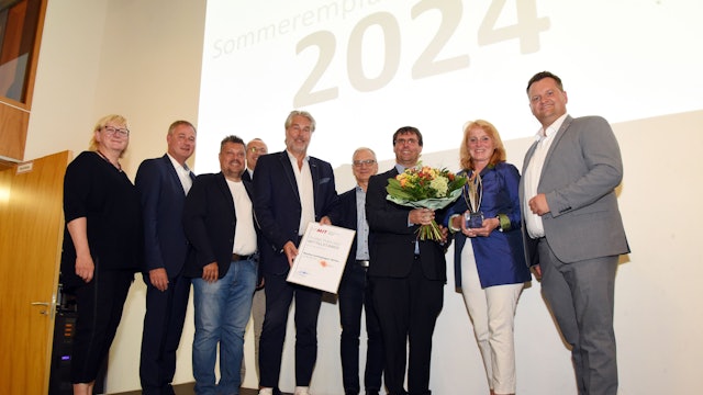 Frauen und Männer stehen in einer Reihe zusammen. Eine Frau hält einen Blumenstrauß und einen Wirtschaftspreis in den Händen.