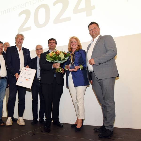 Frauen und Männer stehen in einer Reihe zusammen. Eine Frau hält einen Blumenstrauß und einen Wirtschaftspreis in den Händen.