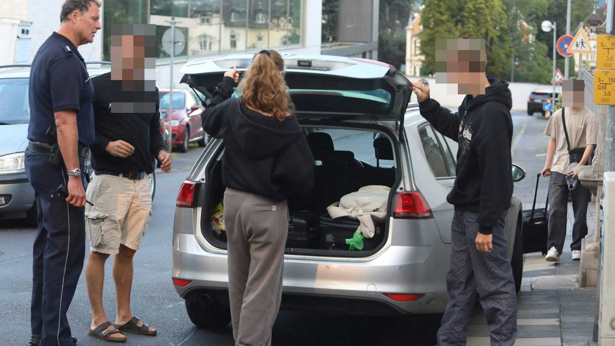 Vier Personen, darunter ein Polizeibeamter, stehen an einem Auto, dessen Heckklappe geöffnet ist.
