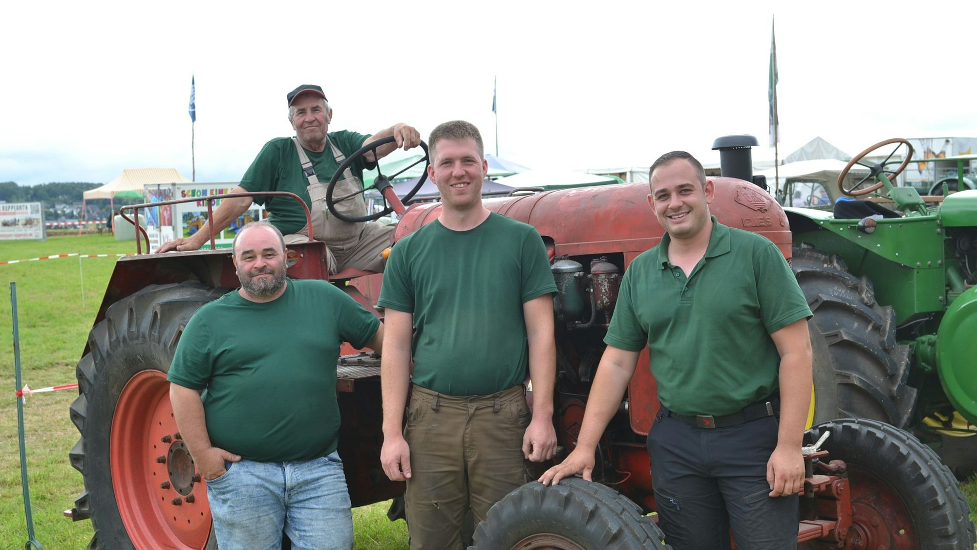 Die drei Männer stehen vor dem roten Schlepper, auf dem Ludwig Blankenheim sitzt. Alle lachen in die Kamera.