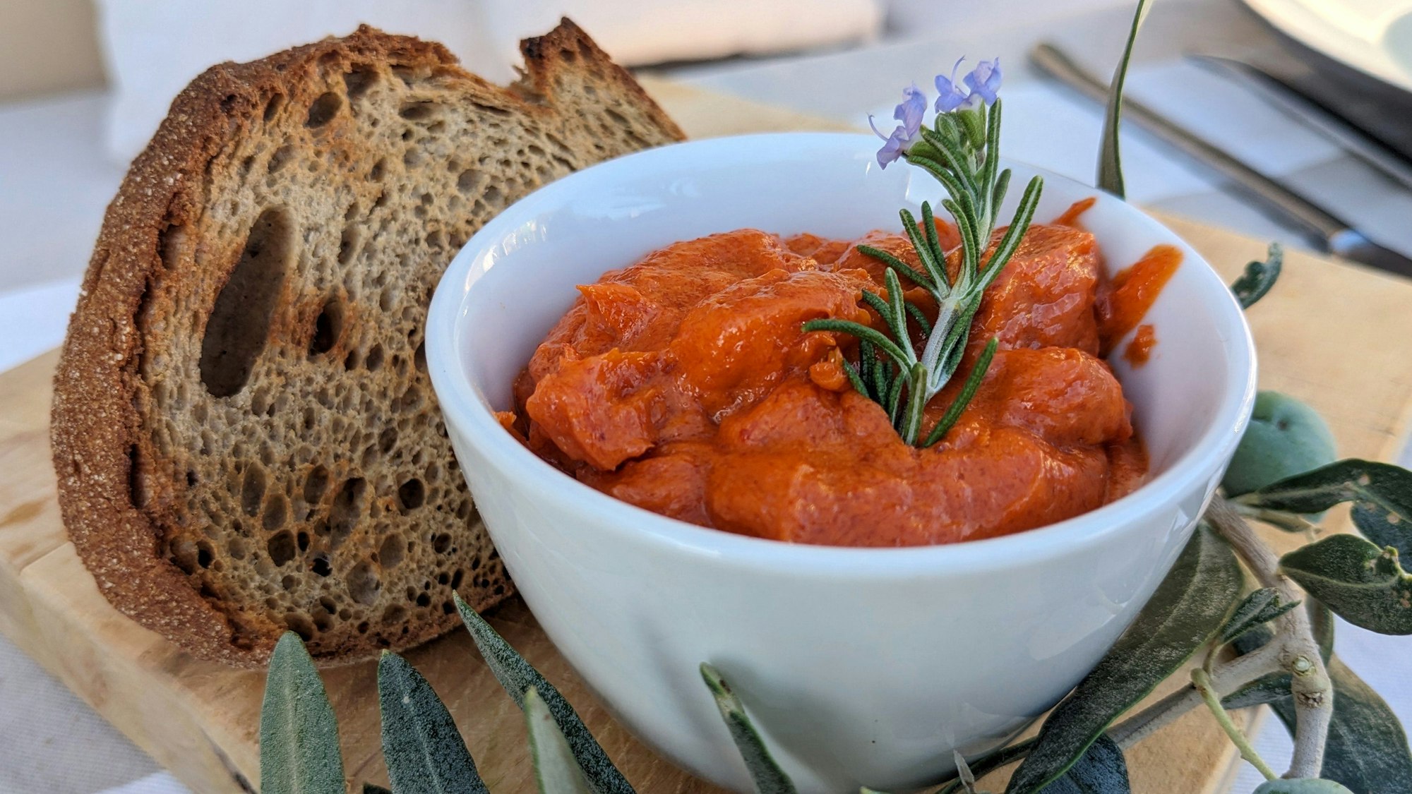 Eine kleine Schale mit Tomatenbutter steht mit einer Scheibe Brot auf einem Brettchen