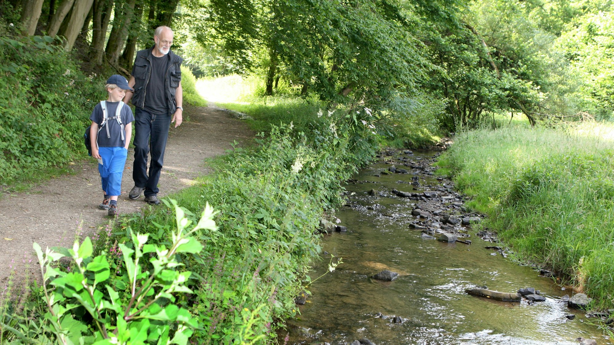 Ein Mann und ein Kind gehen am Bechbach entlang auf einem Wanderweg.
