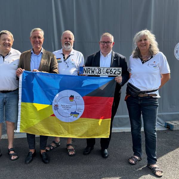 Norbert Röttgen MdB, Gunther Maassen (Vorsitzender von Sankt Augustin and friends hilft e.V.) und Sascha Lienesch MdL hinter der Fahne, mit weiteren Mitgliedern des Vereins, Ukraine