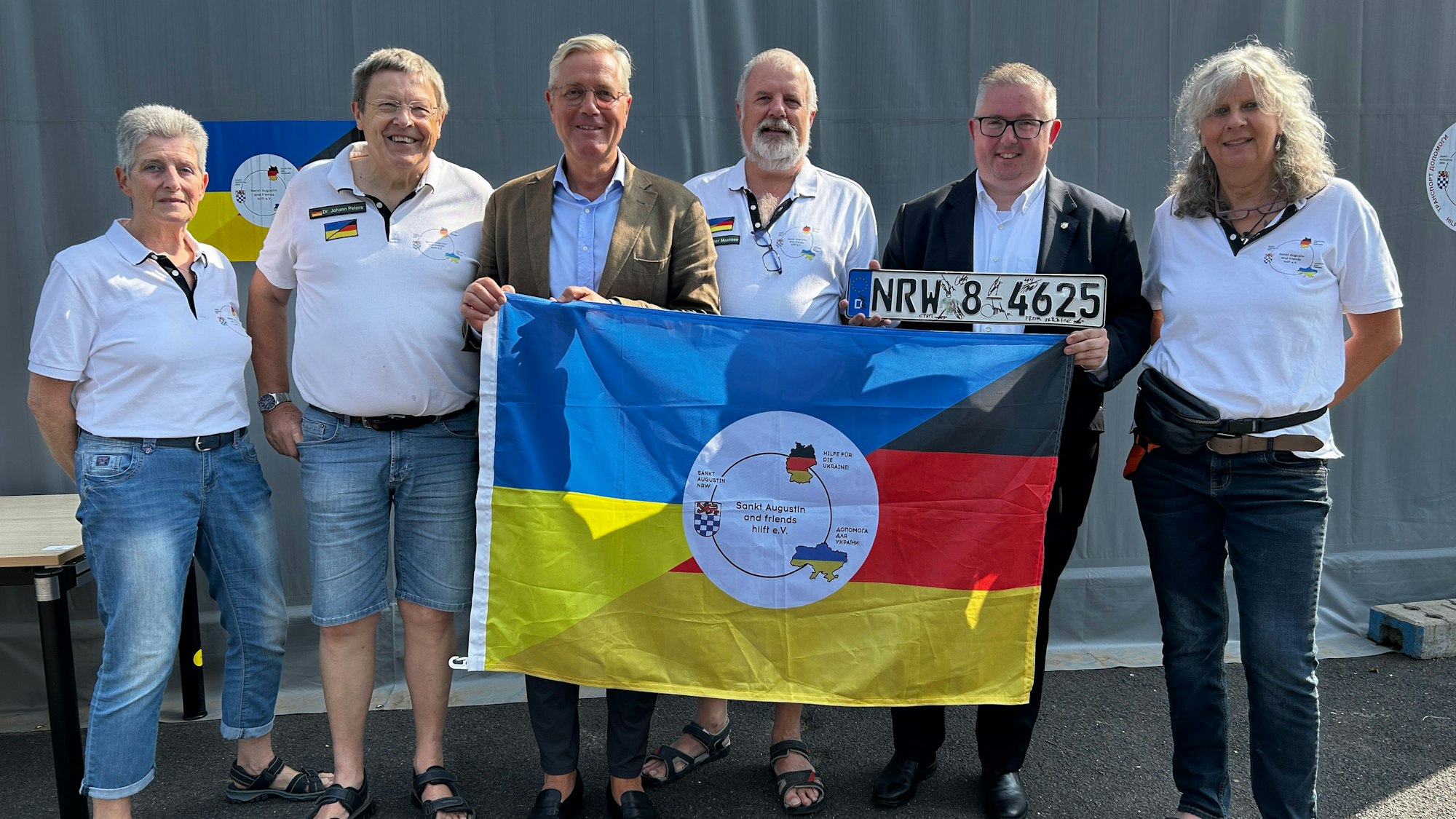 Norbert Röttgen MdB, Gunther Maassen (Vorsitzender von Sankt Augustin and friends hilft e.V.) und Sascha Lienesch MdL hinter der Fahne, mit weiteren Mitgliedern des Vereins, Ukraine