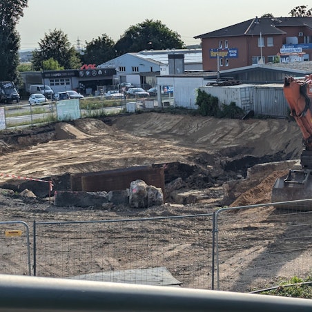 Das Foto zeigt einen Bagger neben einer großen Baugrube.