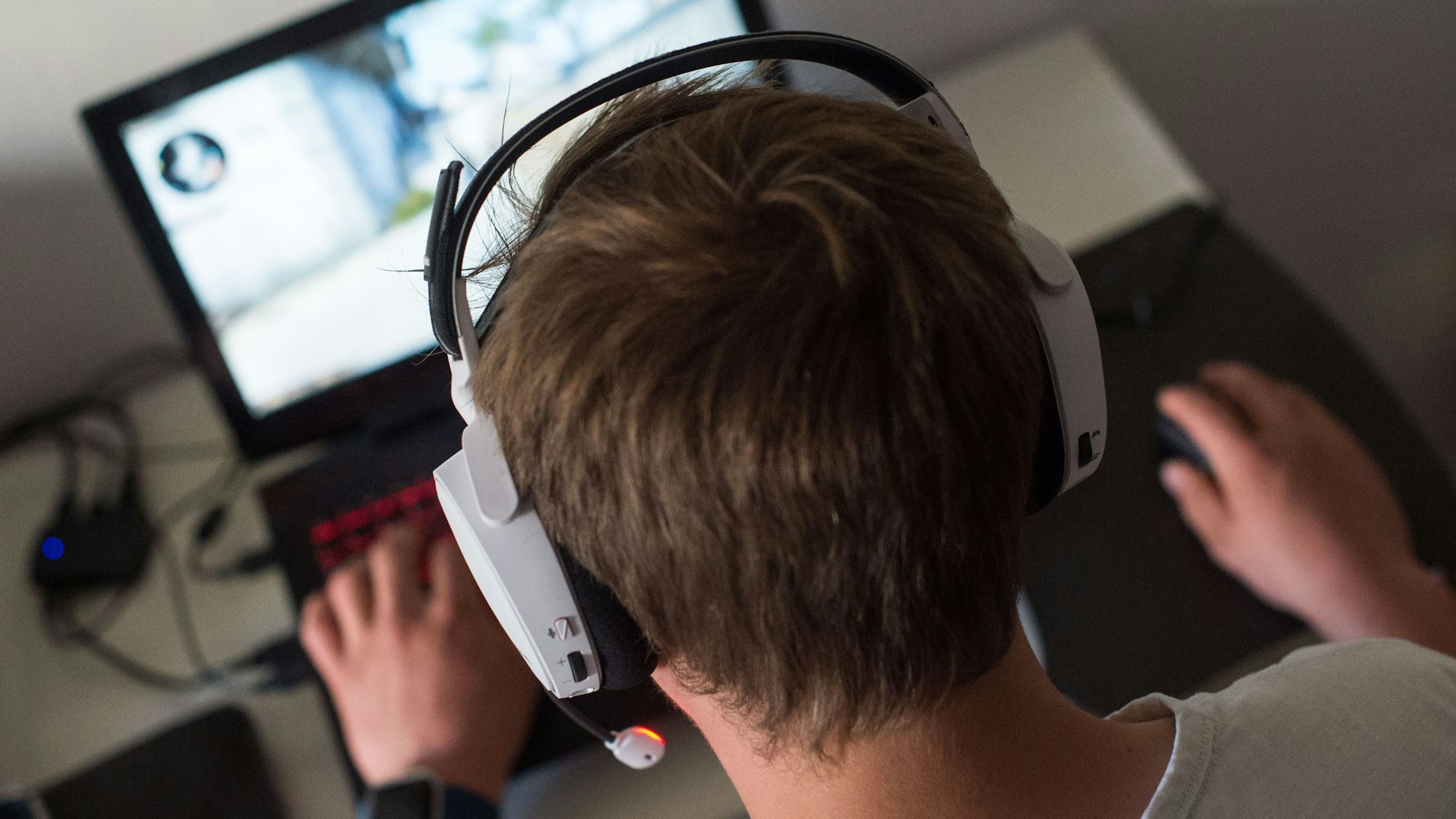Ein Jugendlicher sitzt mit einem Headset vor einem Laptop und spielt ein Online-Computerspiel.