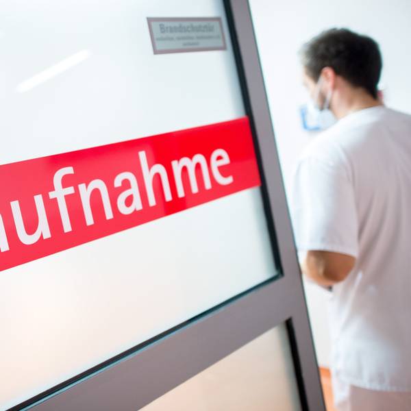 Ein Krankenpfleger steht in einem Krankenhaus neben einer Glastür mit der Aufschrift Notaufnahme.