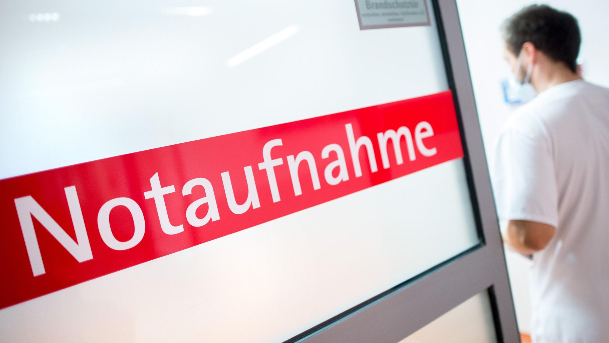 Ein Krankenpfleger steht in einem Krankenhaus neben einer Glastür mit der Aufschrift Notaufnahme.