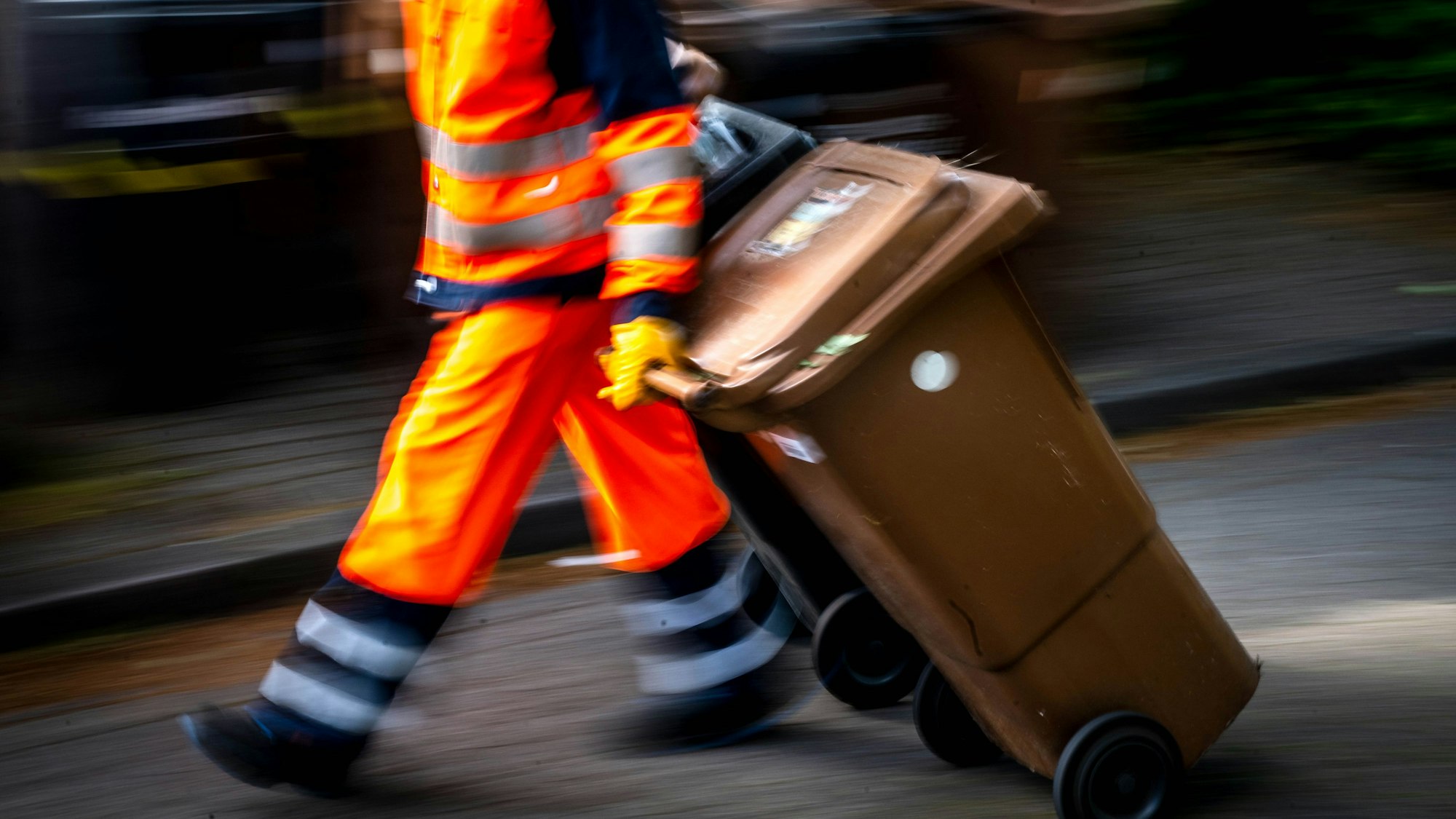 Auf dem Bild ist ein Mitarbeiter der Müllabfuhr zu sehen, der Mülltonnen zieht.