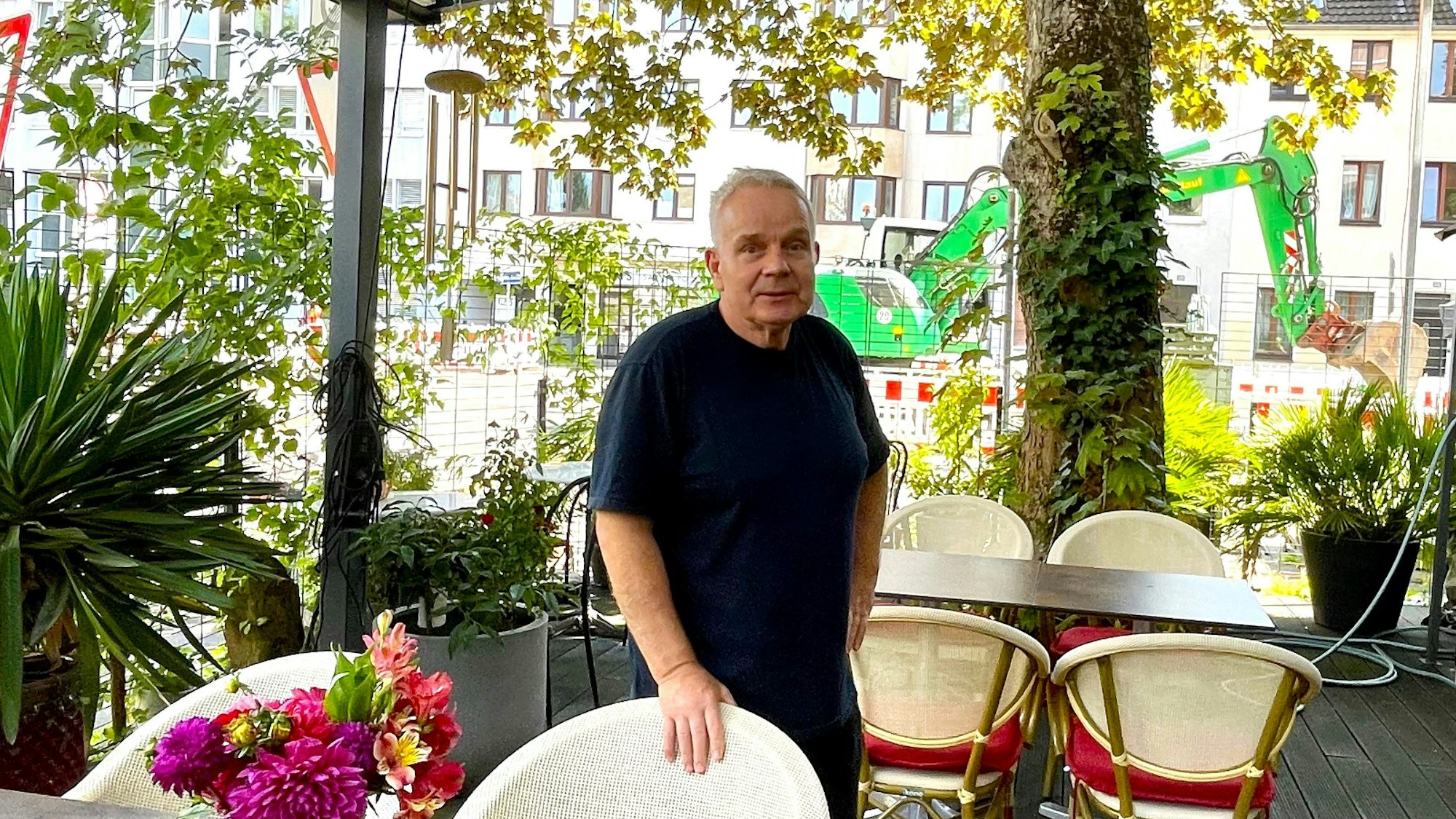 Hartmut Richter steht auf seiner Gartenterrasse, im Hintergrund steht ein Bagger.