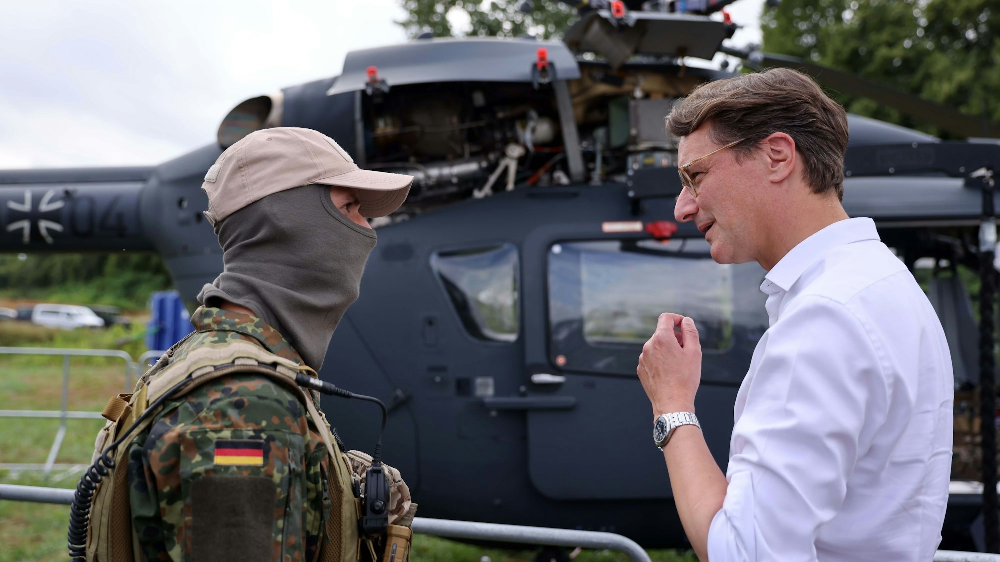 Hendrik Wüst ist im Gespräch mit einem Mann, der in Bundeswehrkleidung bekleidet ist und eine Sturmhaube trägt.