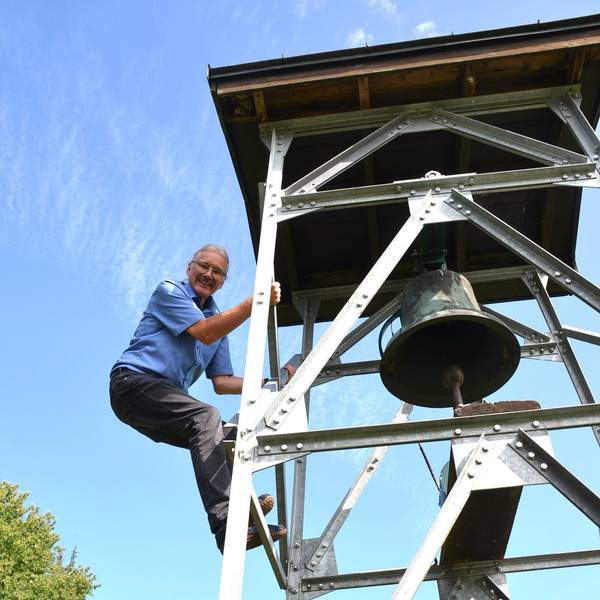 Der kleine Friedhof in der Waldbröler Ortschaft Seifen hat jetzt einen Glockenturm. Dieser stammt aus dem Nachbarort Helten. Pfarrer Thomas Seibel klettert hinauf, um die Inschrift auf der Glocke zu entziffern.