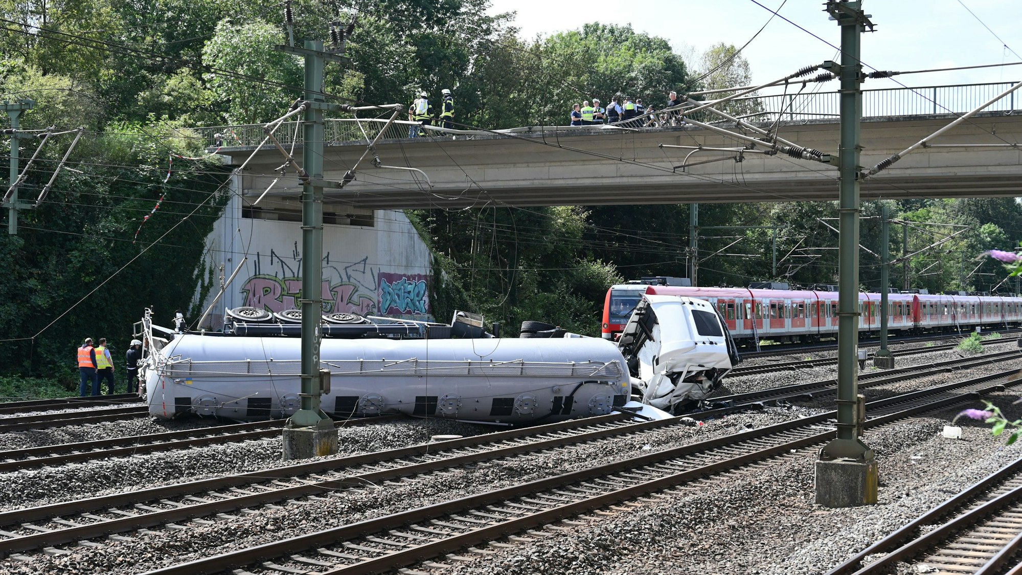 Ein Lkw liegt nach einem Sturz von einer Brücke auf Bahngleisen.
