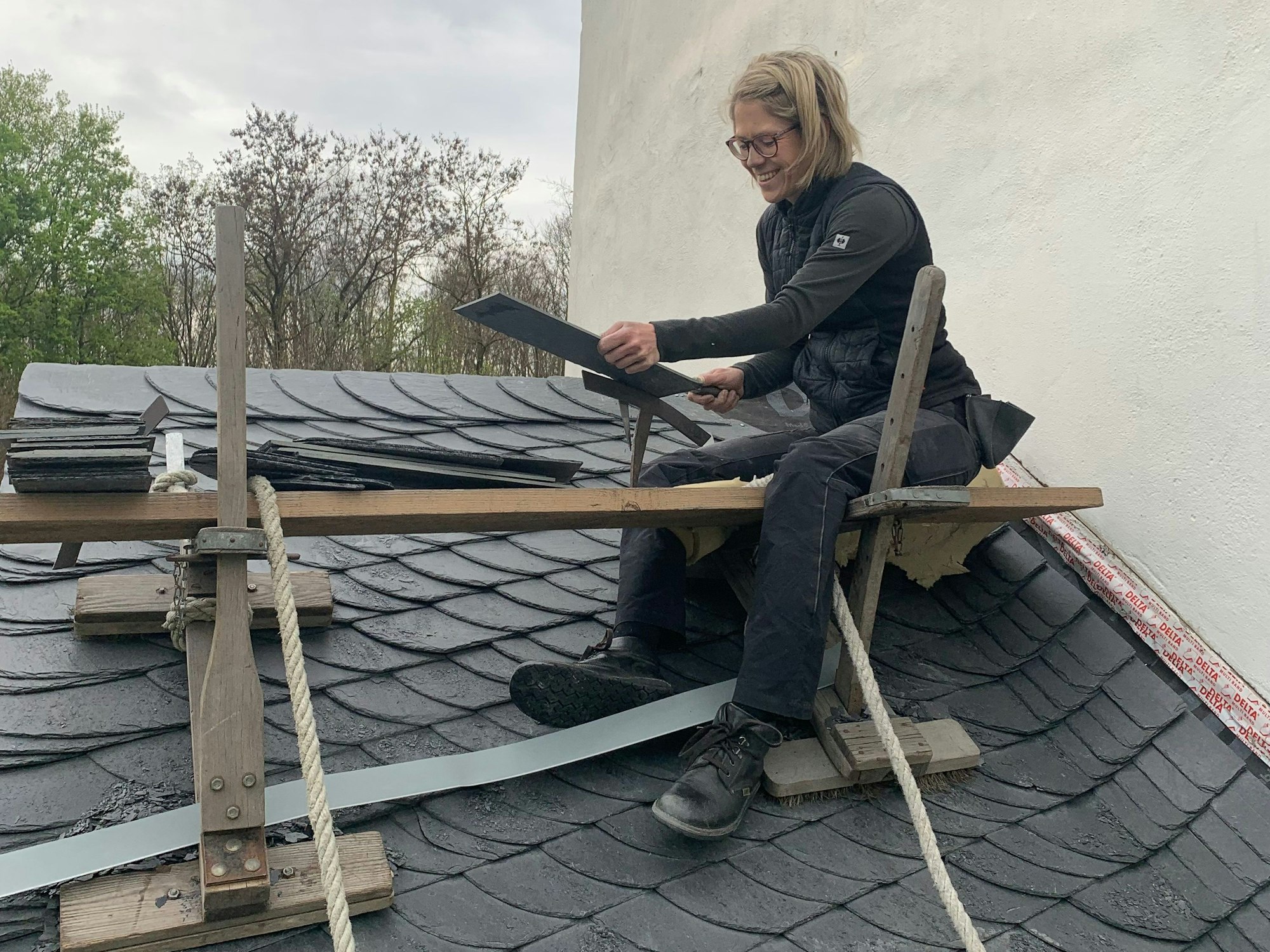 Eine Handwerkerin arbeitet auf einem Schieferdach.