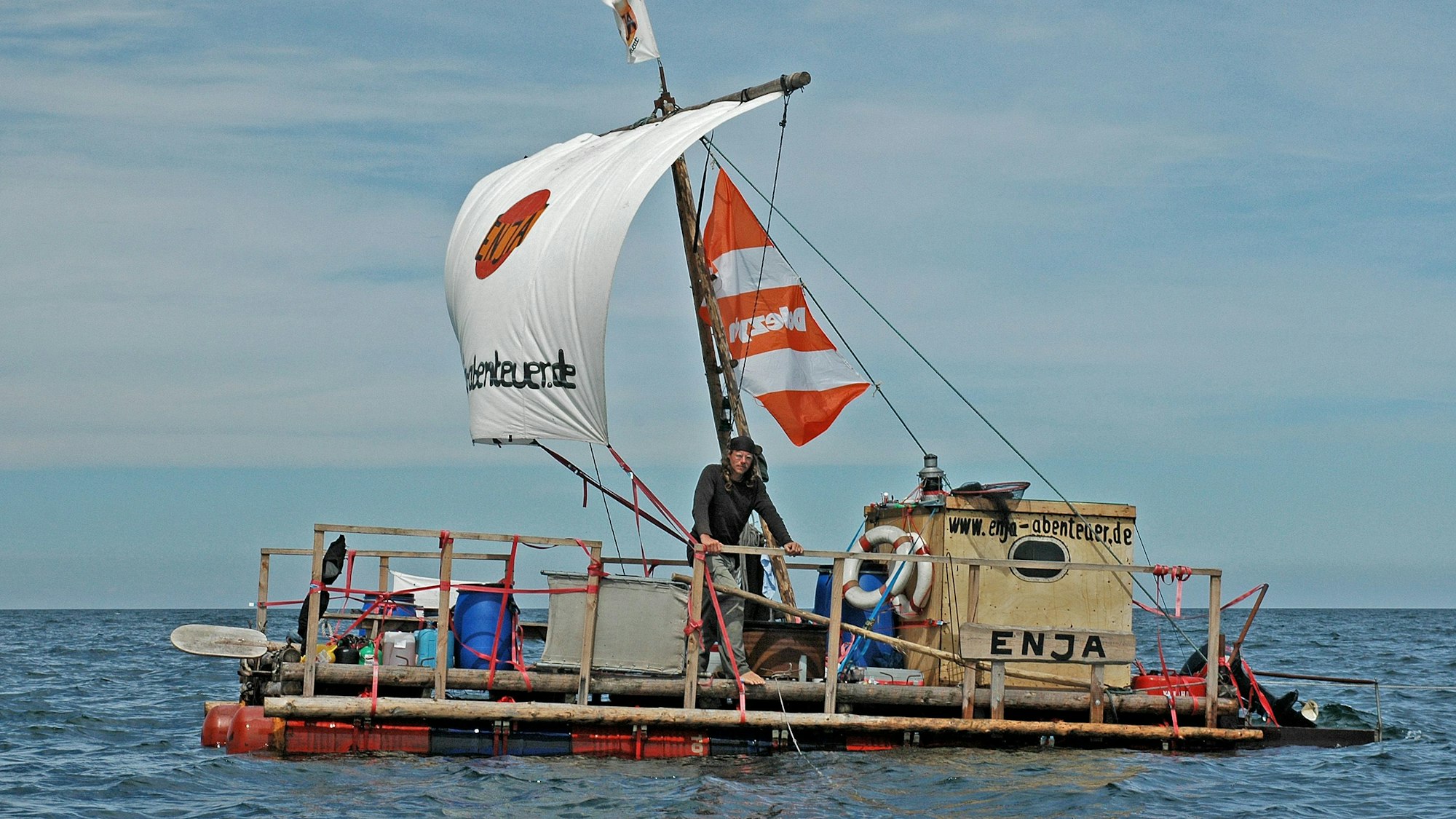 Auf dem Bild ist der Elbepirat Jürgen Schütte auf einem floßartigen Segelschiff auf dem Meer unterwegs.
