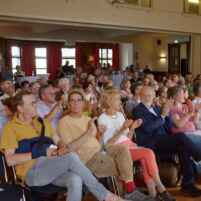 Die Gäste sitzen in Stuhlreihen im Casino und applaudieren.