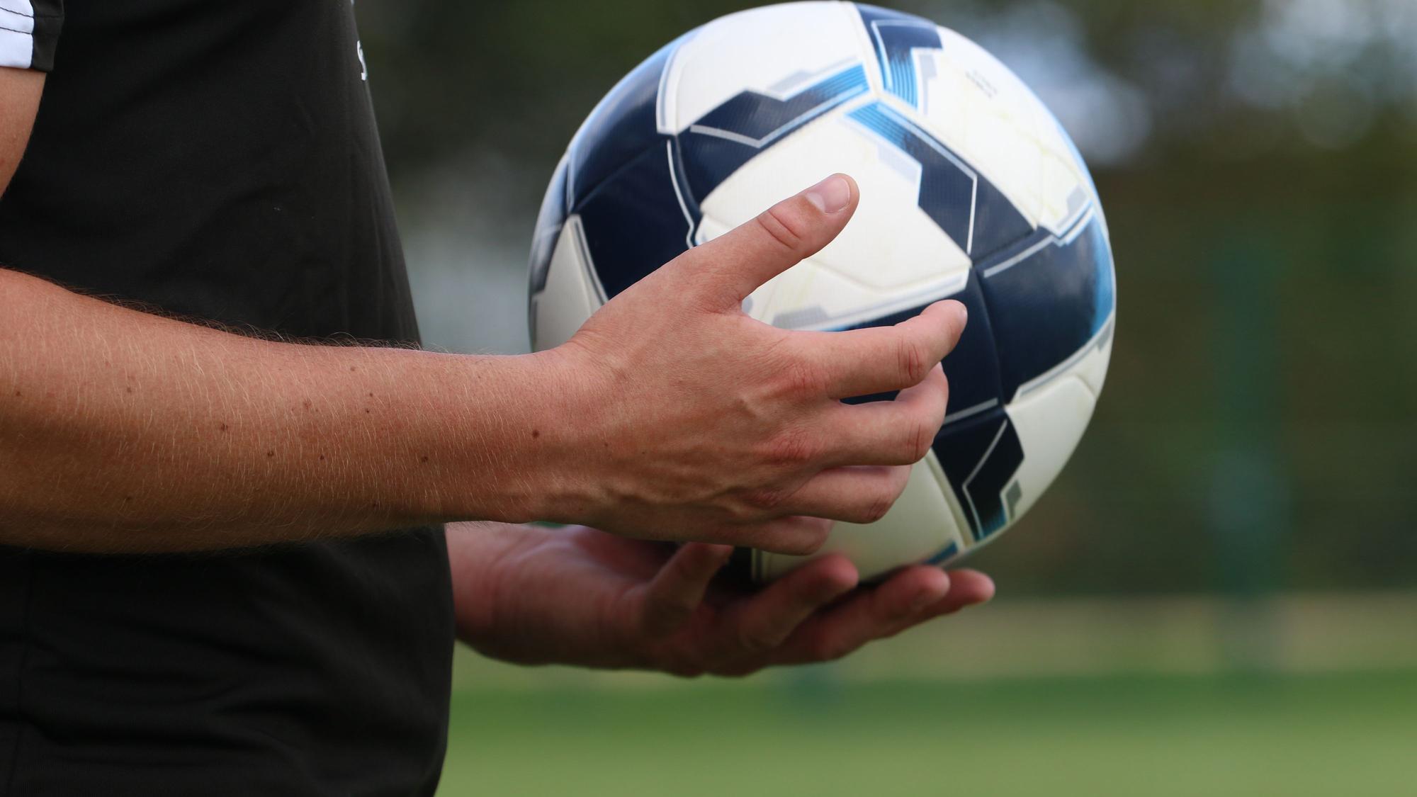 Ein Schiedsrichter hält einen Fußball in der Hand.