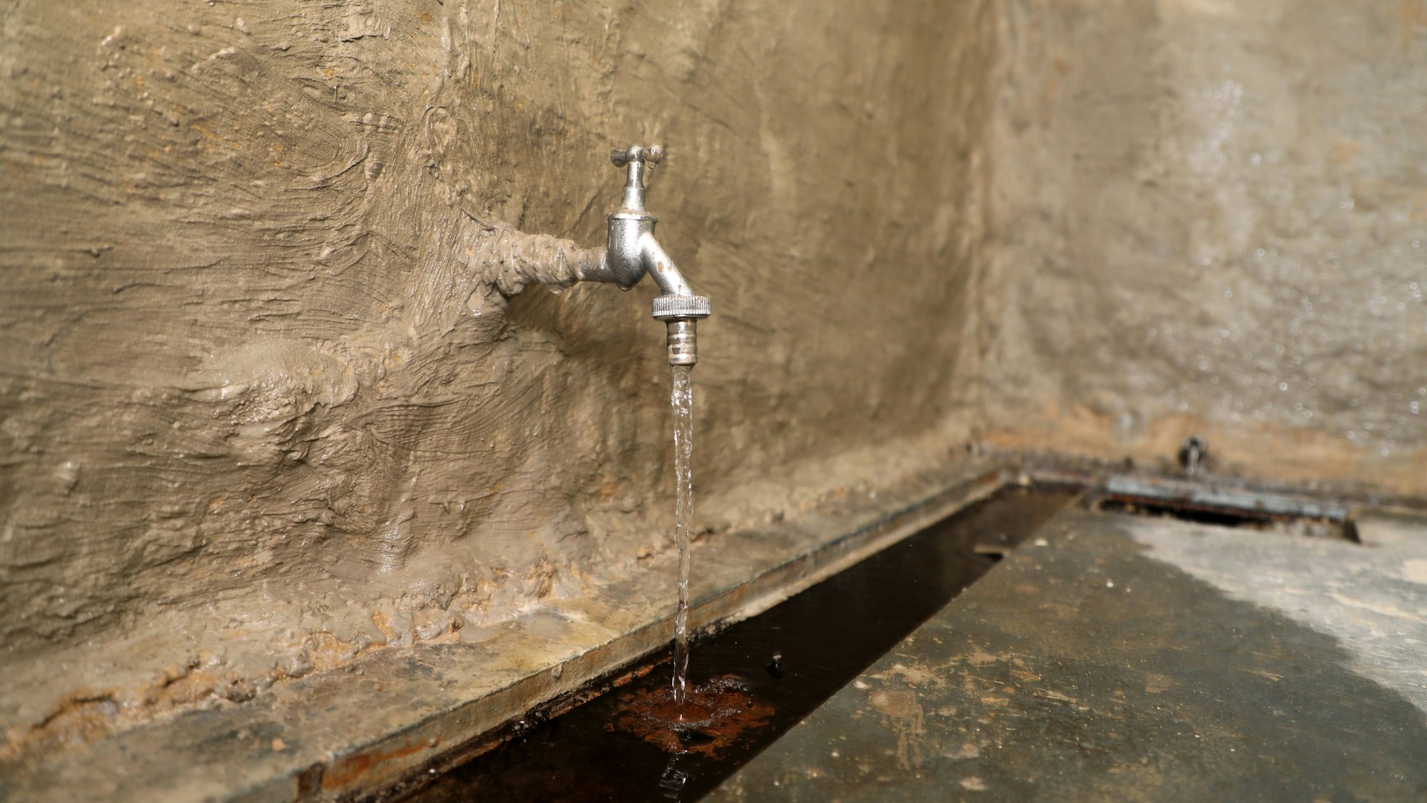Aus einem Wasserhahn in einer Wand des Papiermuseums Alte Dombach in Bergisch Gladbach fließt Wasser.