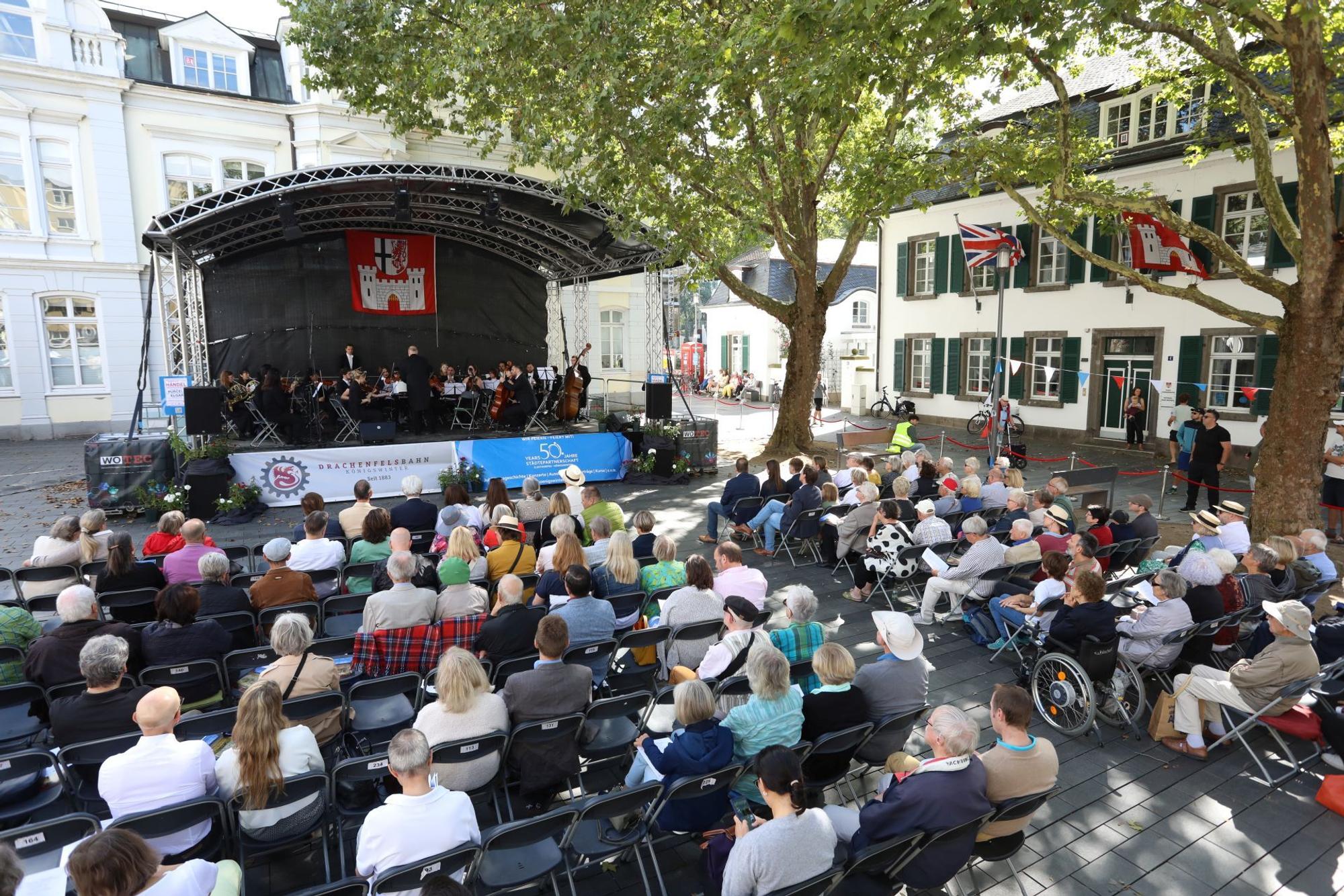 Musiker auf einer Bühne,davor sitzen Menschen auf Stühlen.