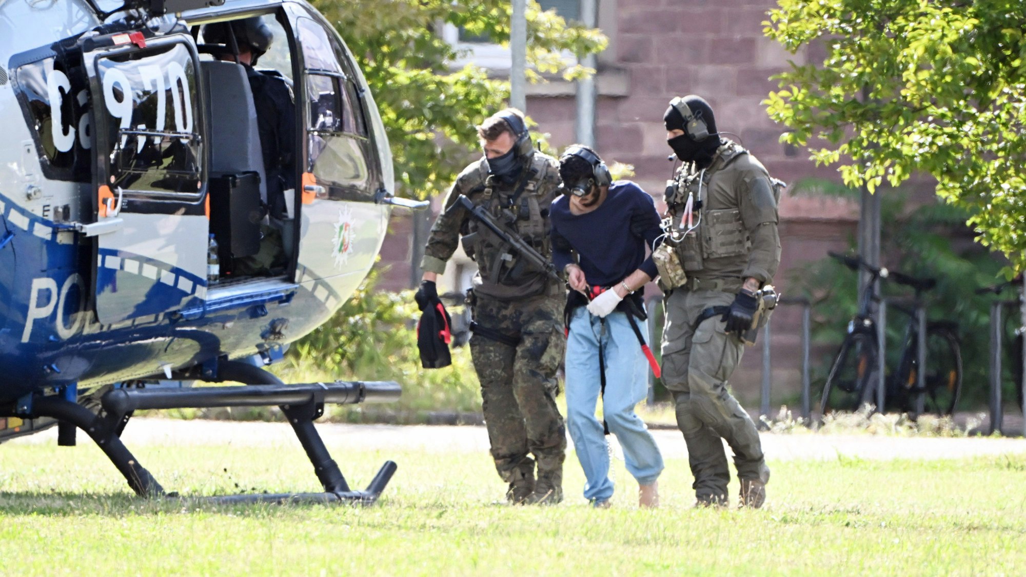 25.08.2024, Baden-Württemberg, Karlsruhe: Der mutmassliche Täter des Messerangriffs von Solingen wird zu einem Hubschrauber gebracht. Zuvor war der Verdächtige dem Ermittlungsrichter beim Bundesgerichtshof (BGH) vorgeführt worden, der Haftbefehl erlassen hat. Foto: Uli Deck/dpa +++ dpa-Bildfunk +++