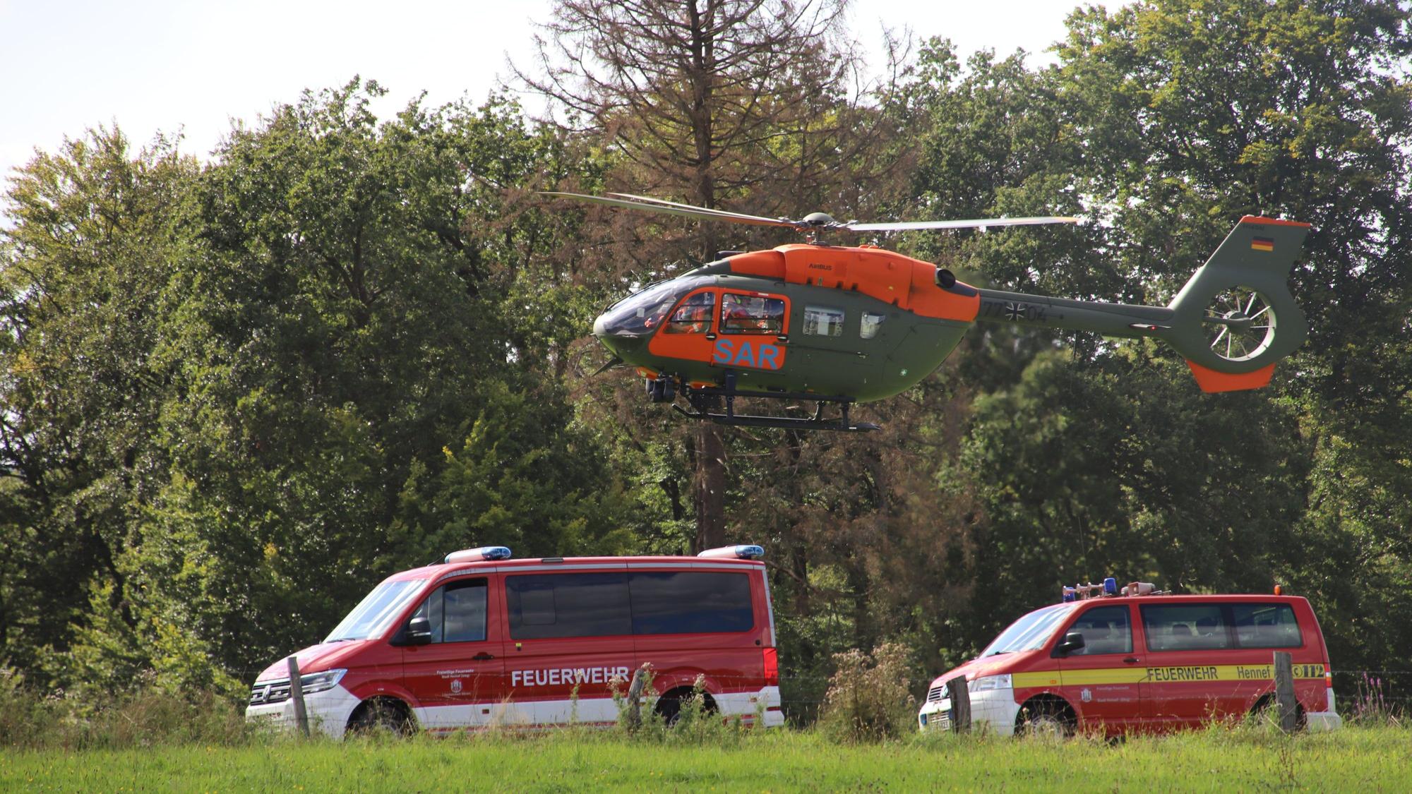 Ein Hubschrauber landet hinter zwei Feuerwehrfahrzeugen.