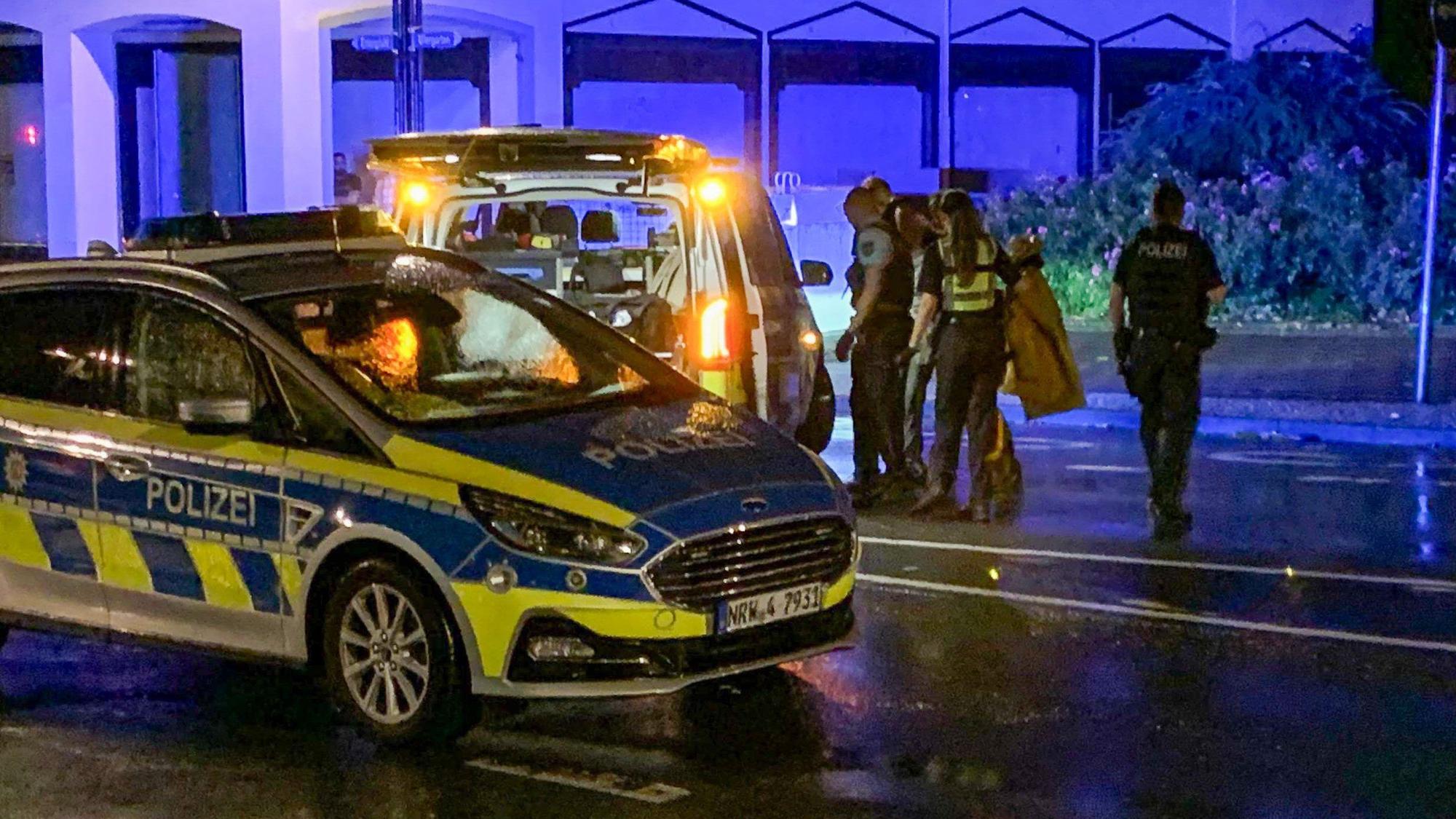 Es sind zwei Fahrzeuge der Polizei zu sehen und mehrere Menschen.