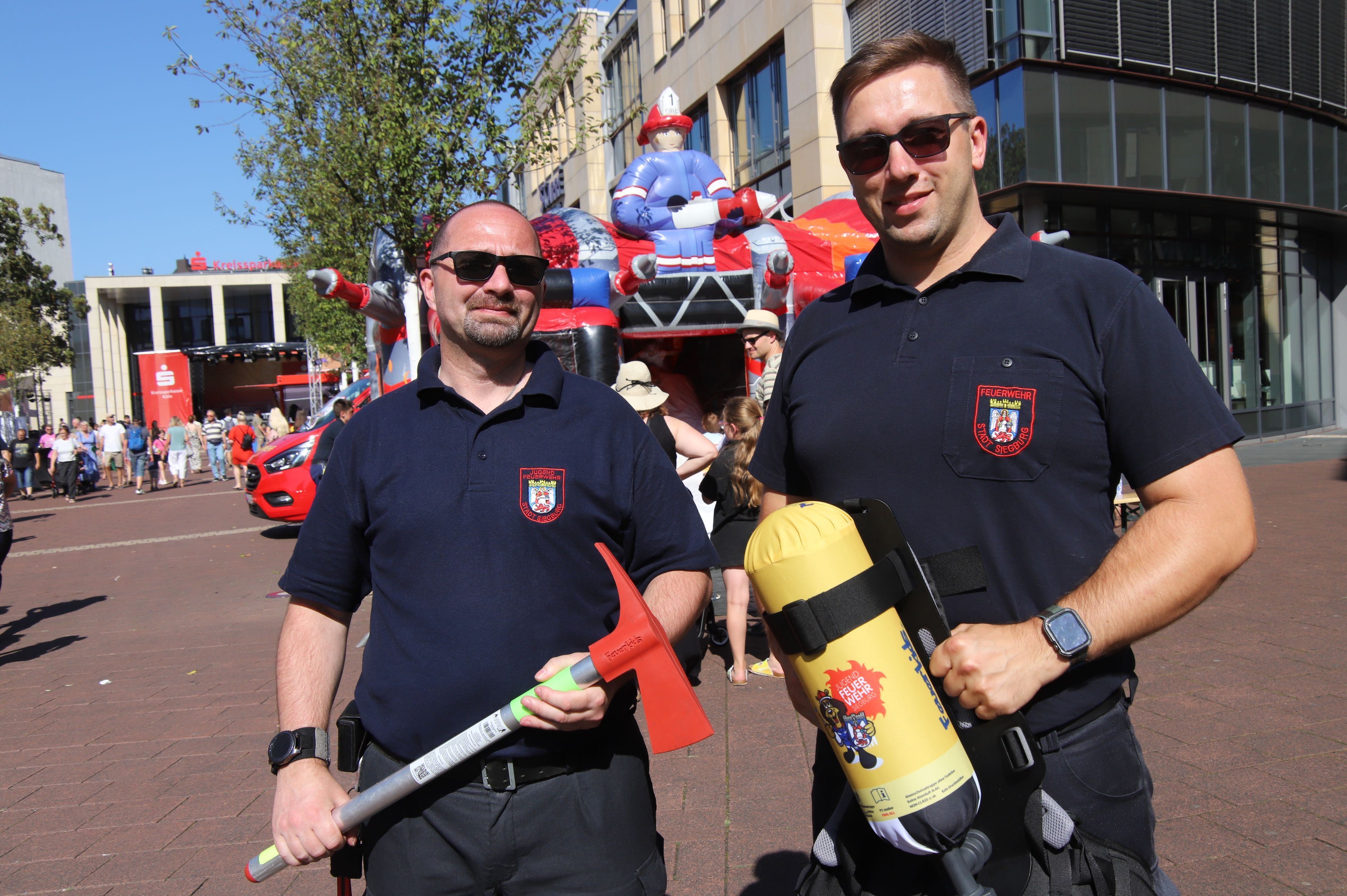 Zwei Feuerwehrleute präsentieren kindgerechtes Feuerwehr-Equipment.