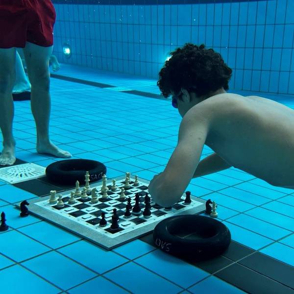 Ein Schachspieler taucht im Schwimmbecken ab, um beim Unterwasserschach einen Zug zu machen.