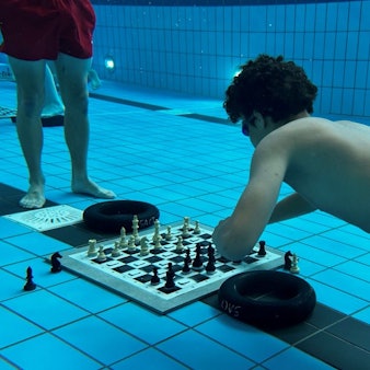Ein Schachspieler taucht im Schwimmbecken ab, um beim Unterwasserschach einen Zug zu machen.