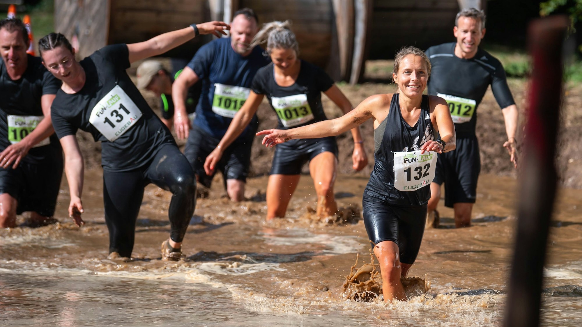 Das Bild zeigt einige Teilnehmende, die eine Grube mit Schlammwasser meistern.