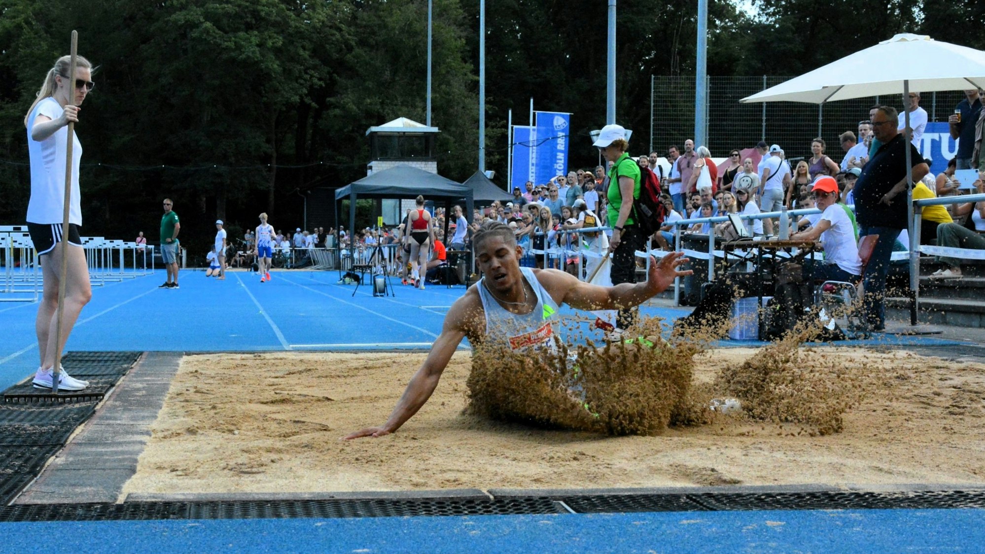 Ein Weitspringer landet in der Grube und Sand spritzt auf.