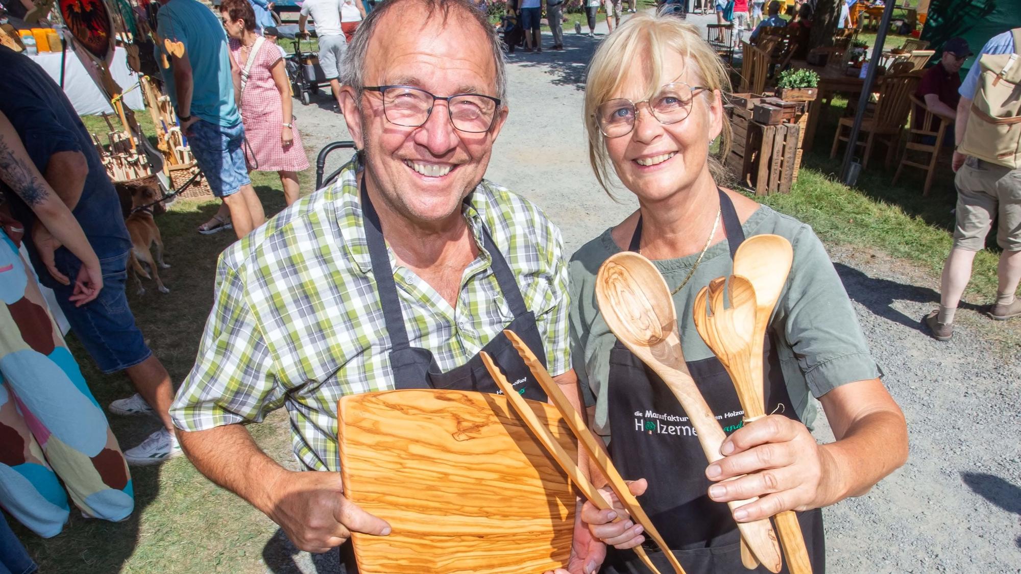 Ein Mann und eine Frau präsentieren Küchenbesteck aus Holz auf einem Markt.