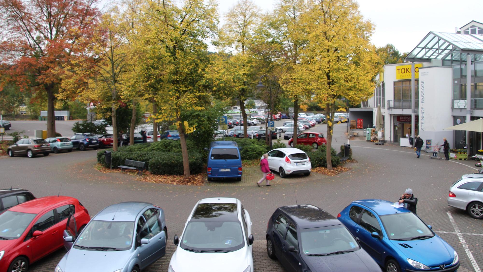 Auf dem Overather Steinhofplatz parken Autos, Menschen gehen zum Einkaufen.