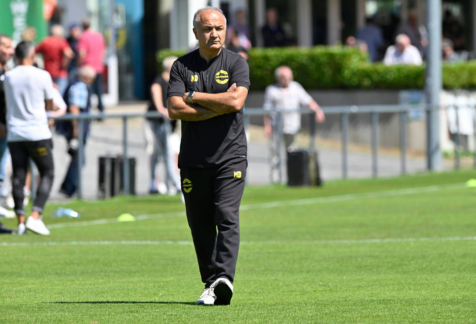 Mutlu Demir, Trainer des SV Eintracht Hohkeppel, geht mit verschränkten Armen und grimmigen Gesicht über den Platz.