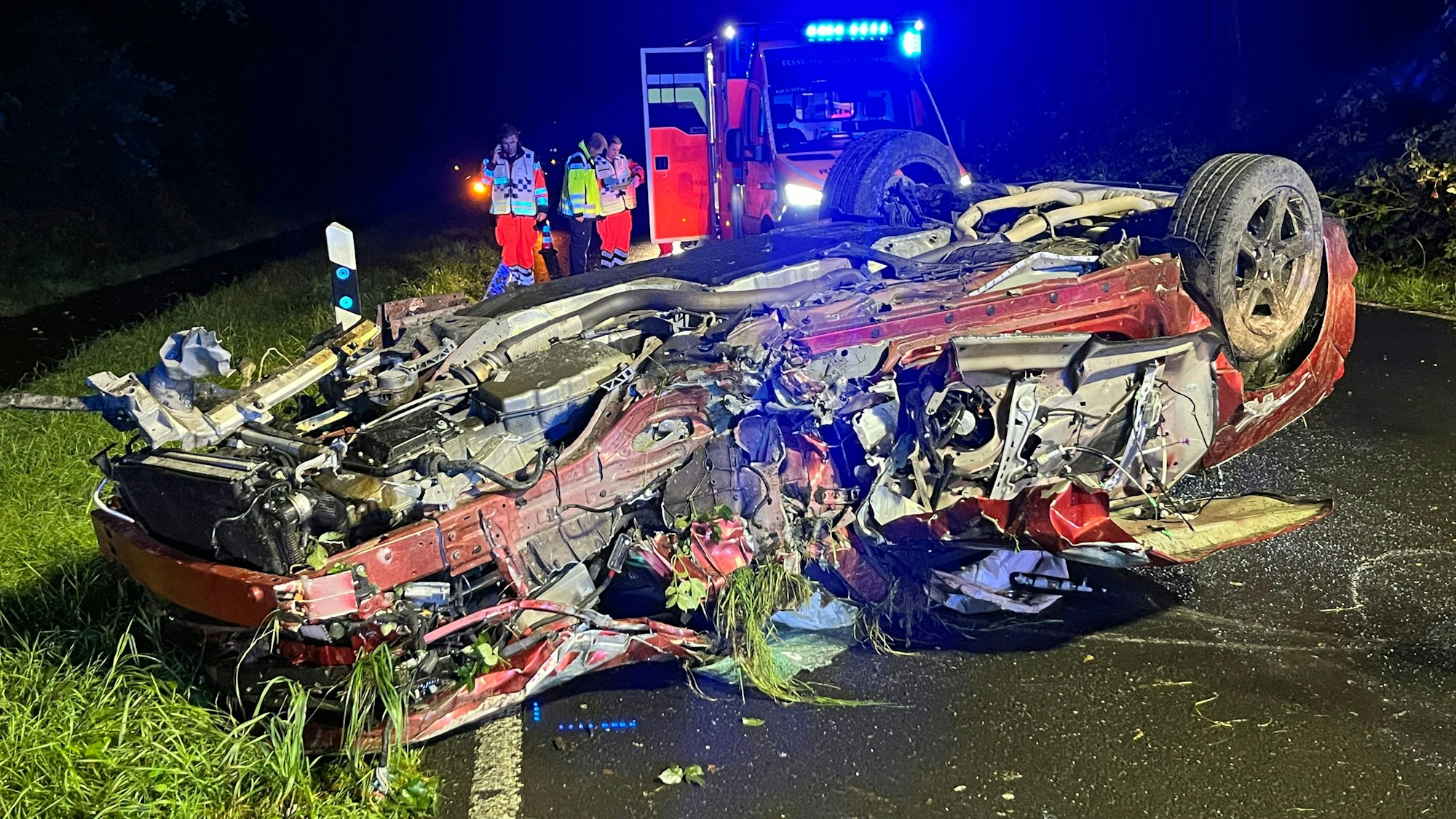 Ein schwer beschädigtes Auto liegt auf dem Dach, dahinter ein Rettungswagen, in dem ein Patient behandelt wird