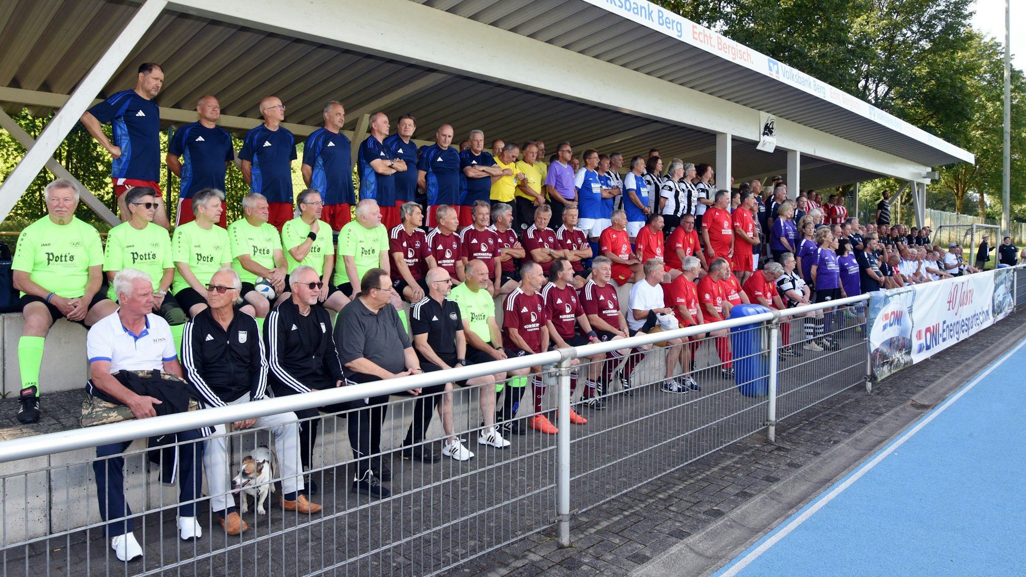 Gruppenbild der Walking-Football-Mannschaften, die auf der Tribüne PLatz genommen haben.