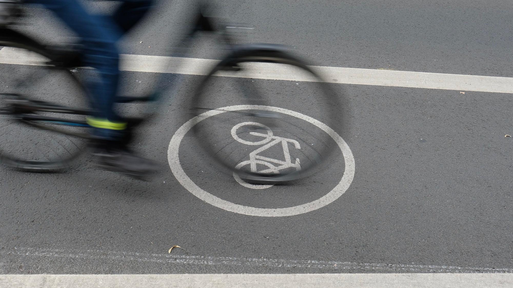 Ein Fahrradfahrer fährt auf dem Radfahrstreifen einer Fahrbahn. Ein Fahrradweg-Piktogramm ist auf der Fahrbahn in Weiß angebracht.