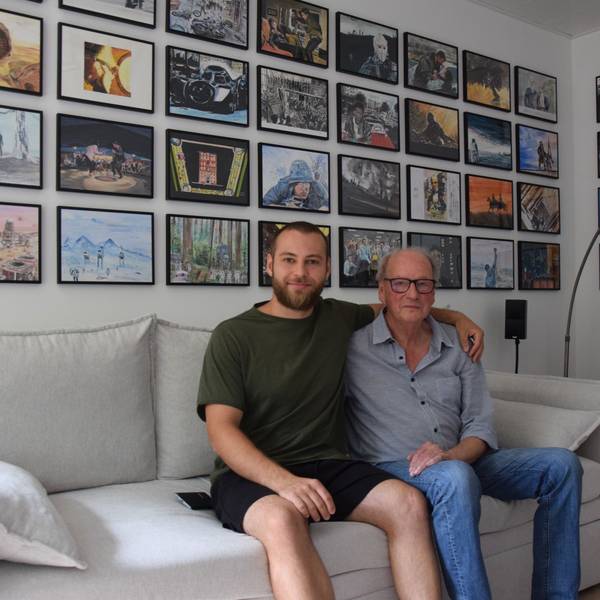 Zu sehen sind Winfried Brück (rechts) und sein Enkel. Sie sitzen auf einer Couch, im Hintergrund hängen eingerahmt die Filmszenen, die Brück für seinen Enkel gemalt hat.