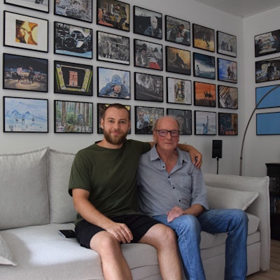 Zu sehen sind Winfried Brück (rechts) und sein Enkel. Sie sitzen auf einer Couch, im Hintergrund hängen eingerahmt die Filmszenen, die Brück für seinen Enkel gemalt hat.