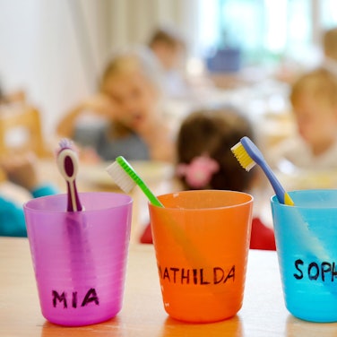 Zahnbürsten und Zahnputzbecher mit den Vornamen der Kinder stehen in einer Kindertagesstätte auf einem Tisch.