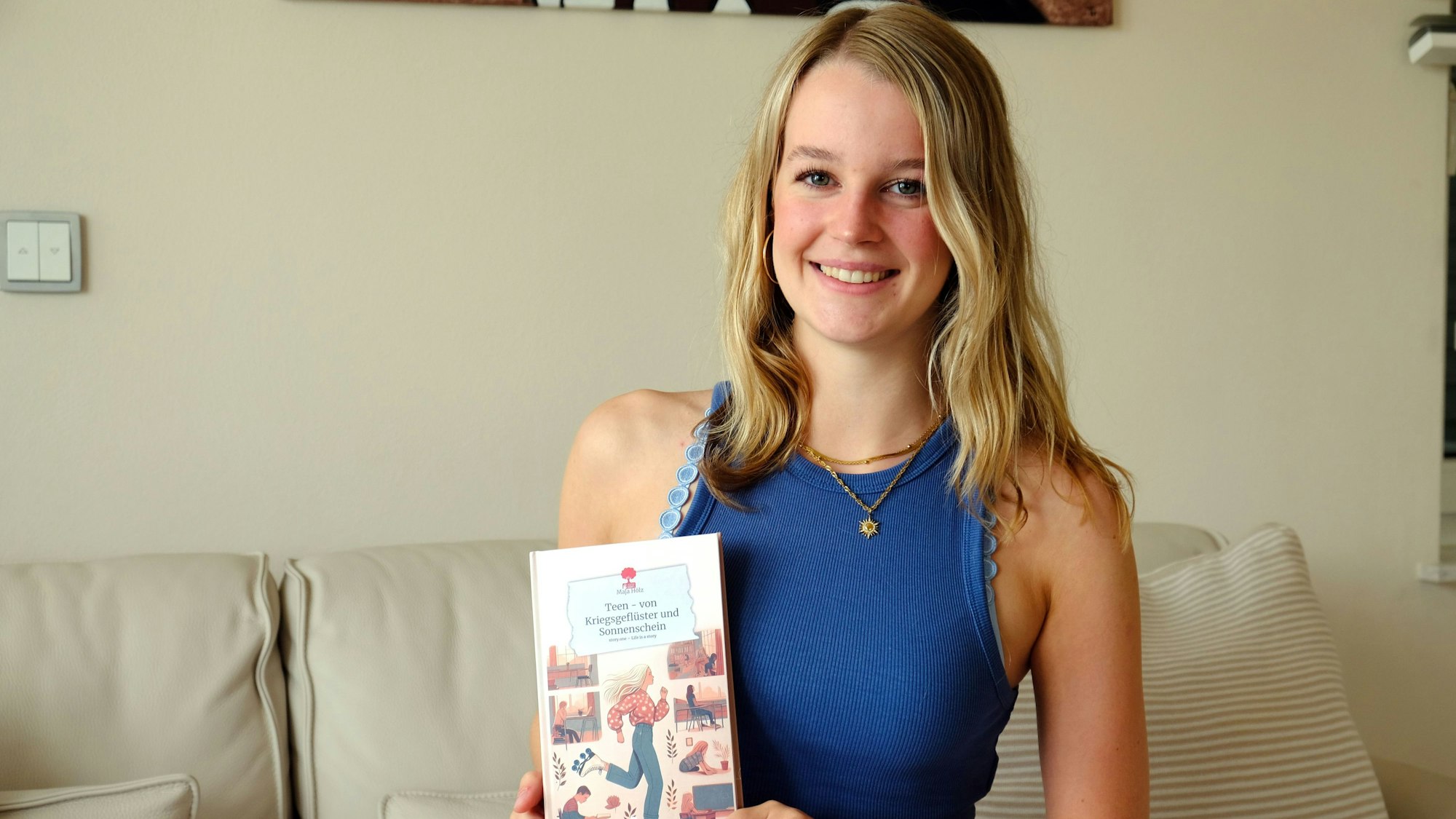 Maja Hölz sitzt auf einem Sofa und hält vor sich ihr Buch.