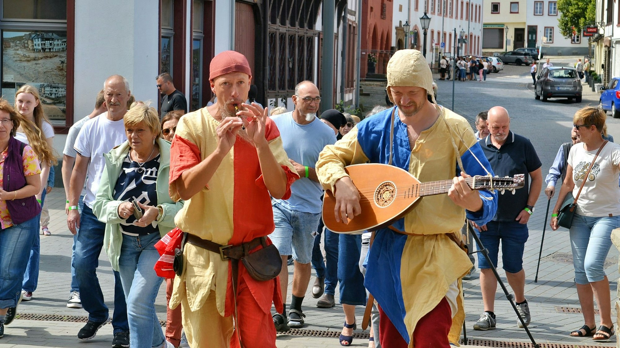 Ein Gauklerduo spielt Flöte und Laute. Im Hintergrund sind einige Zuschauer zu sehen.