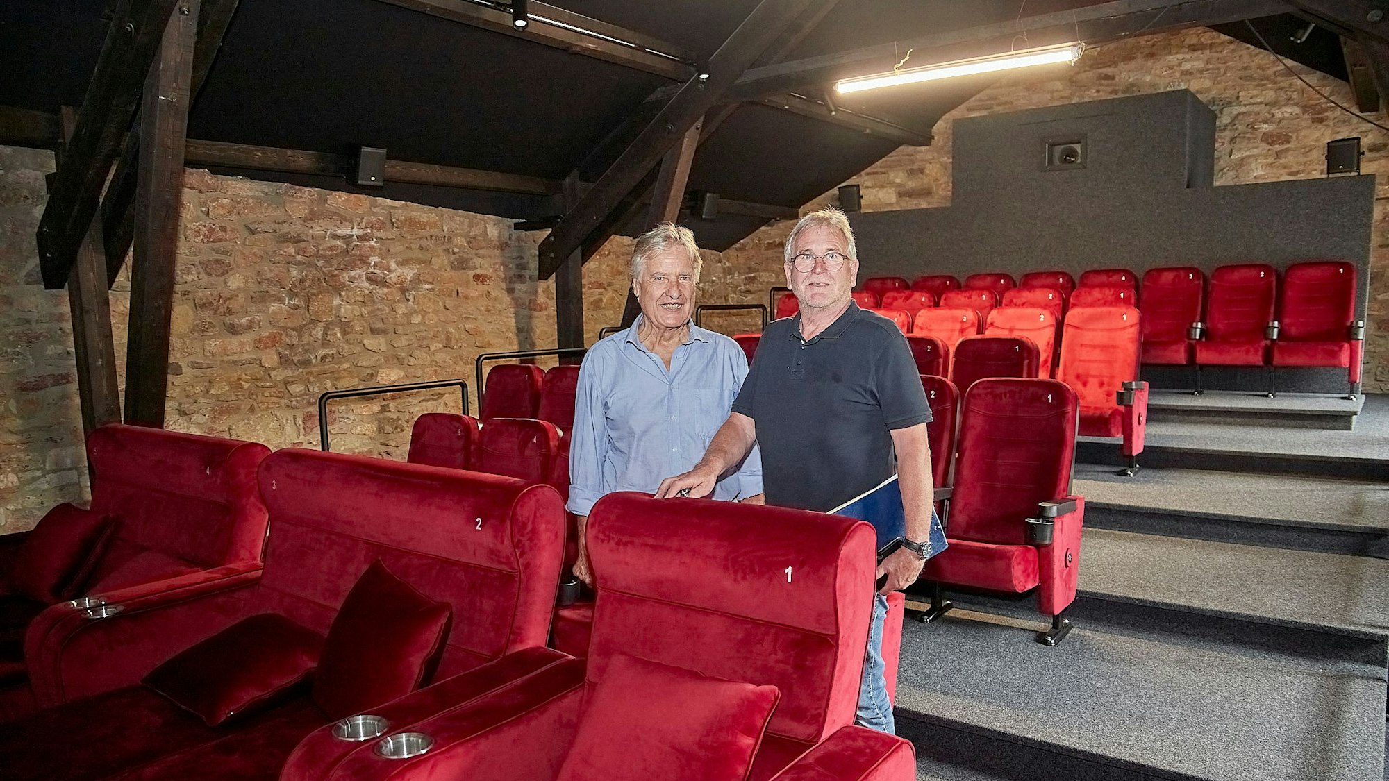 Zwei Männer stehen zwischen zwei Sitzreihen des neuen Kommunalkinos, im Hintergrund Bruchsteinwände.