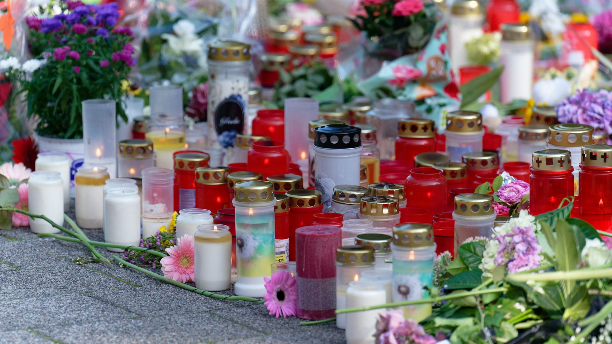 Solingen: Blumen und Kerzen in Gedenken an die Opfer liegen an einer Kirche in der Nähe des Tatorts. Viele Menschen haben Blumen und Kerzen zum Gedenken an die Opfer in der Nähe des Tatorts abgelegt.