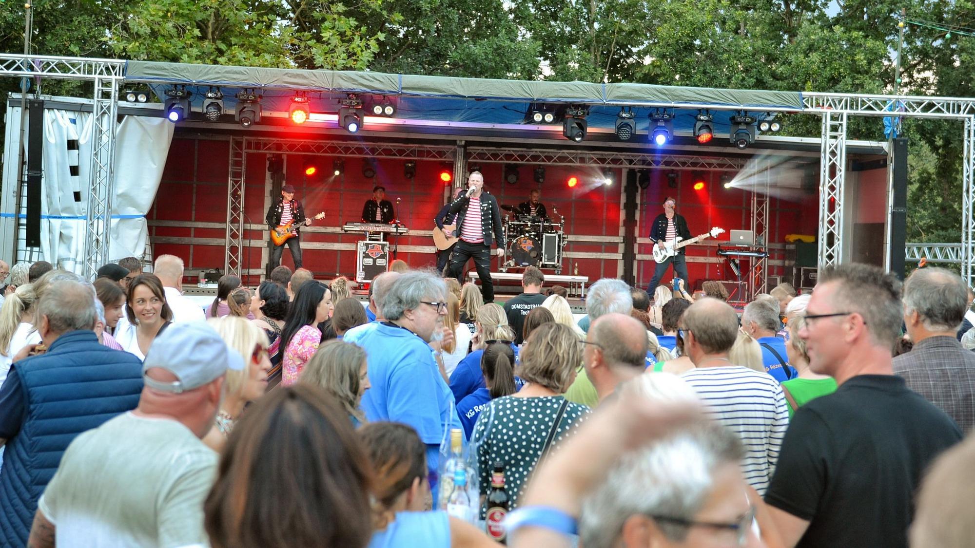 Eine Band spielt auf einer Bühne vor Publikum im Freien.