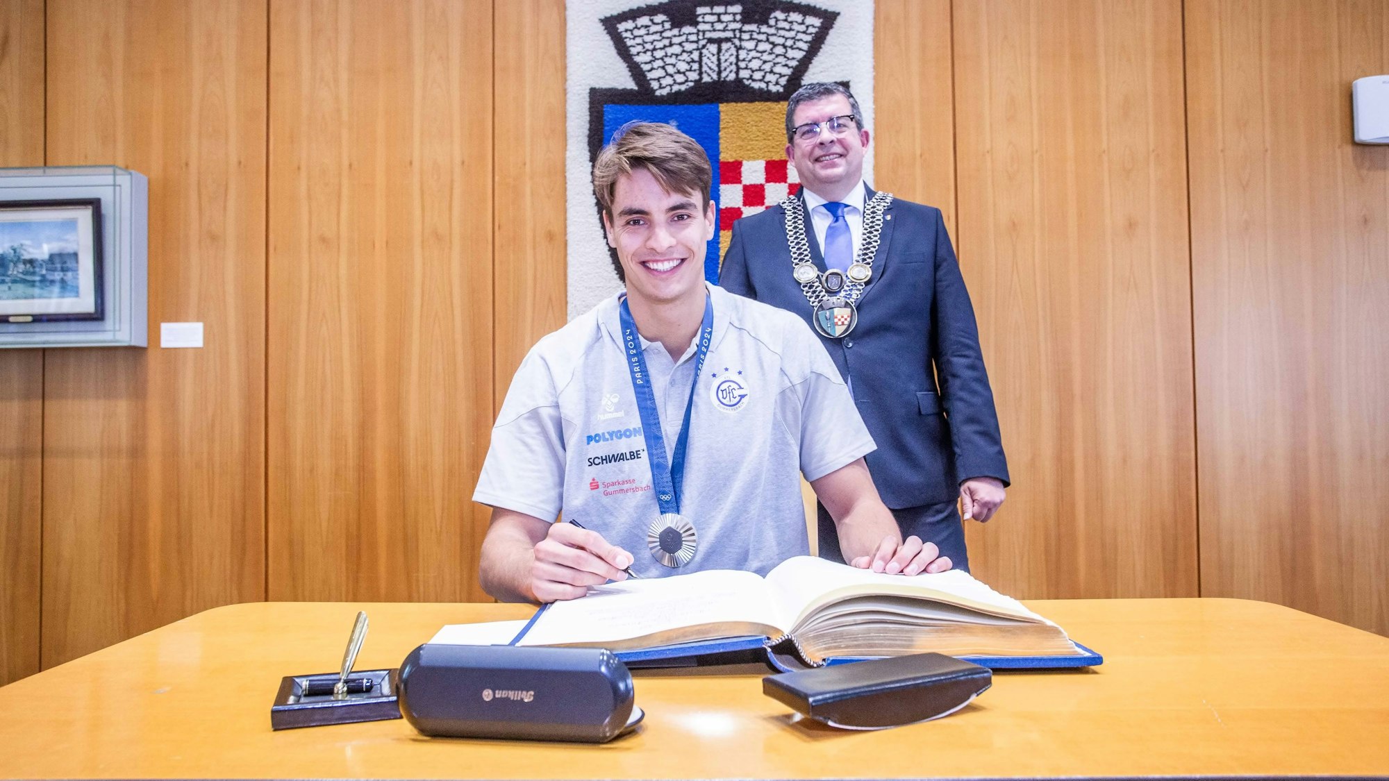 Gummersbachs Kapitän Julian Köster trägt sich in das Goldene Buch der Stadt Gummersbach ein. Hinter ihm steht Bürgermeister Frank Helmenstein.