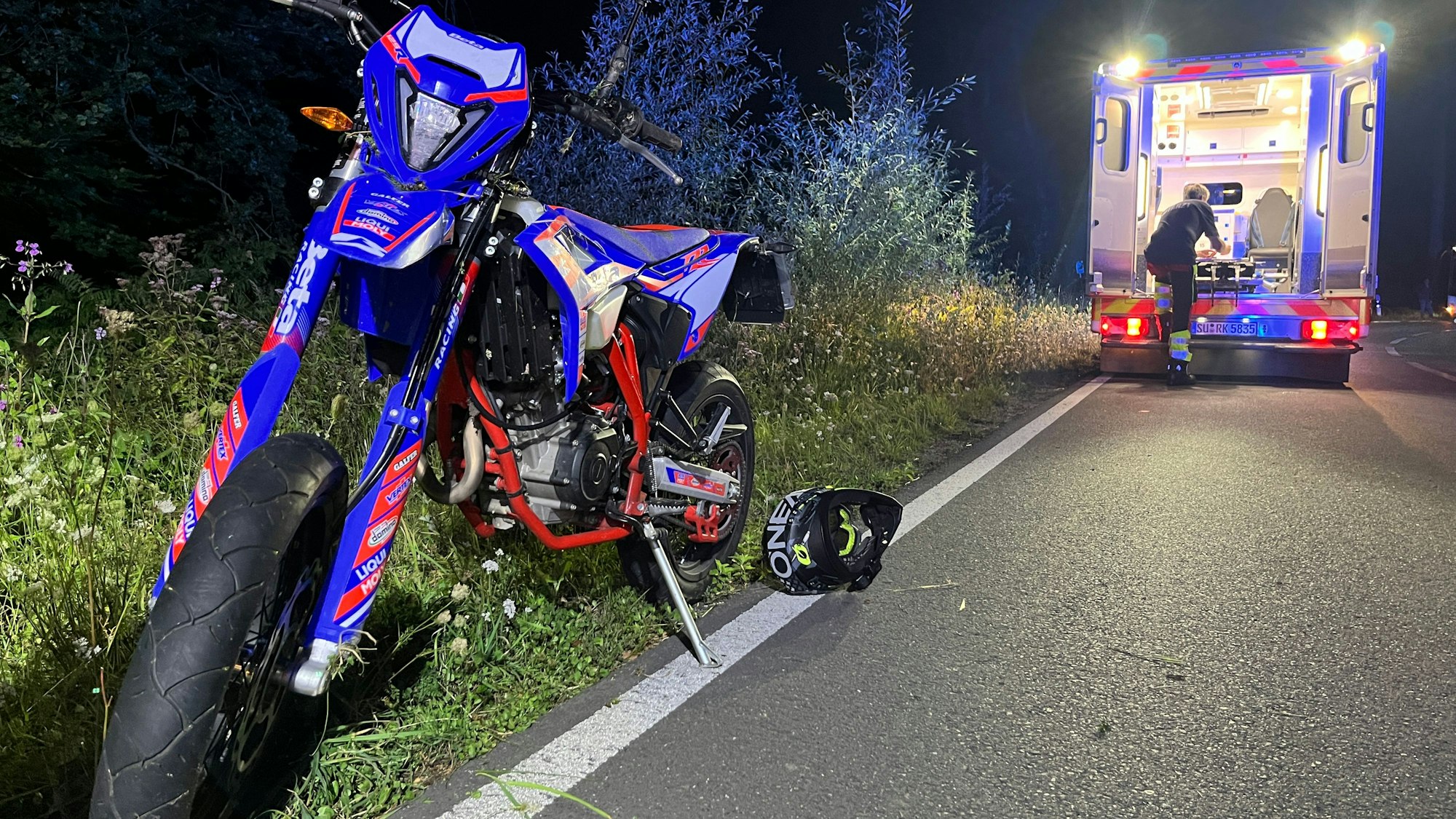 Ein beschädigtes Leichtkradrad steht am Straßenrand neben einem Rettungswagen.
