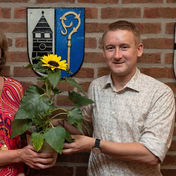 Eine Frau und ein Mann schauen in die Kamera, sie wirkt sehr ernst. Gemeinsam halten sie eine Sonnenblume in die Kamera.